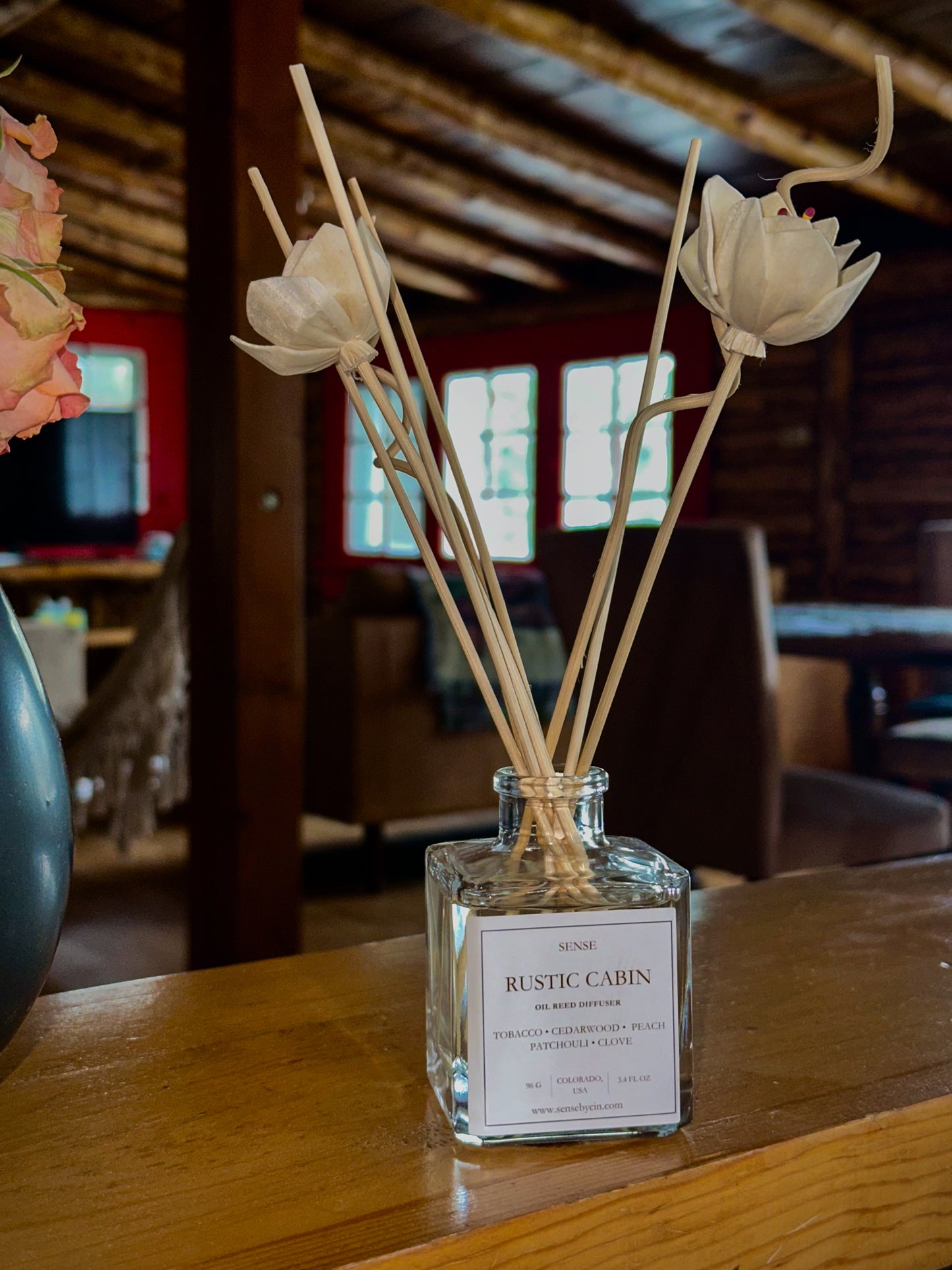 Diffuser with reeds and flowers on a wooden surface in a rustic cabin setting