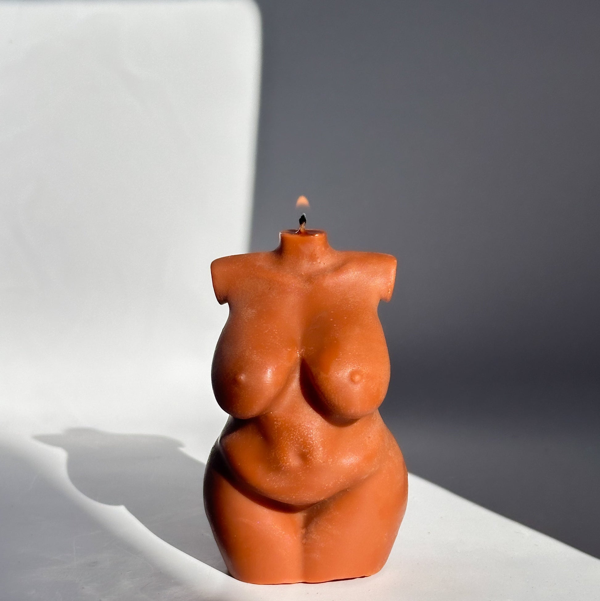 Brown-colored torso-shaped candle on a white surface with a gray background