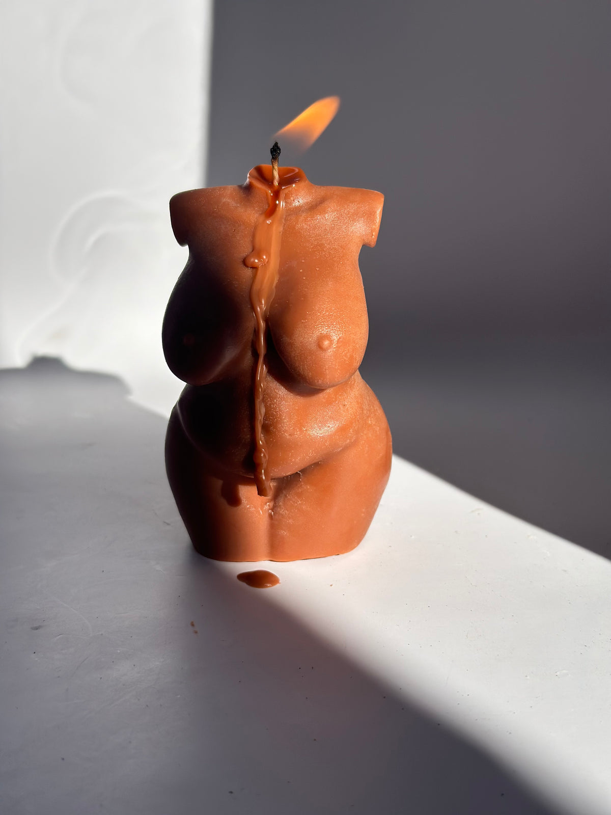 Body shaped candle against a plain background with a shadow going over the top