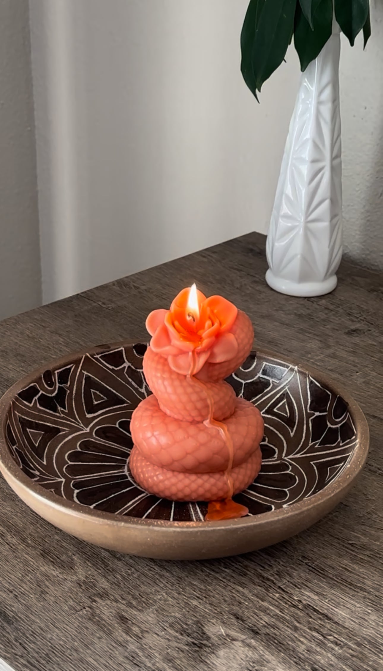 Decorative candle in a bowl on a wooden surface with a white vase in the background